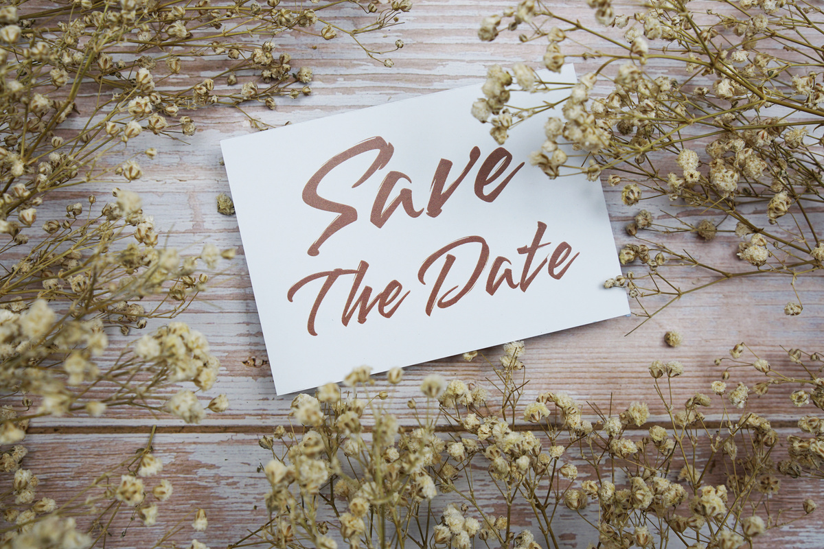 Save the Date text on paper card with flower decoration on wooden background